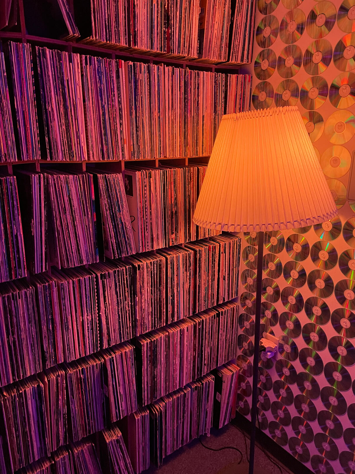 Neon lighting. Lamp against wall of reflective CDs. Filled wall of vinyl records.