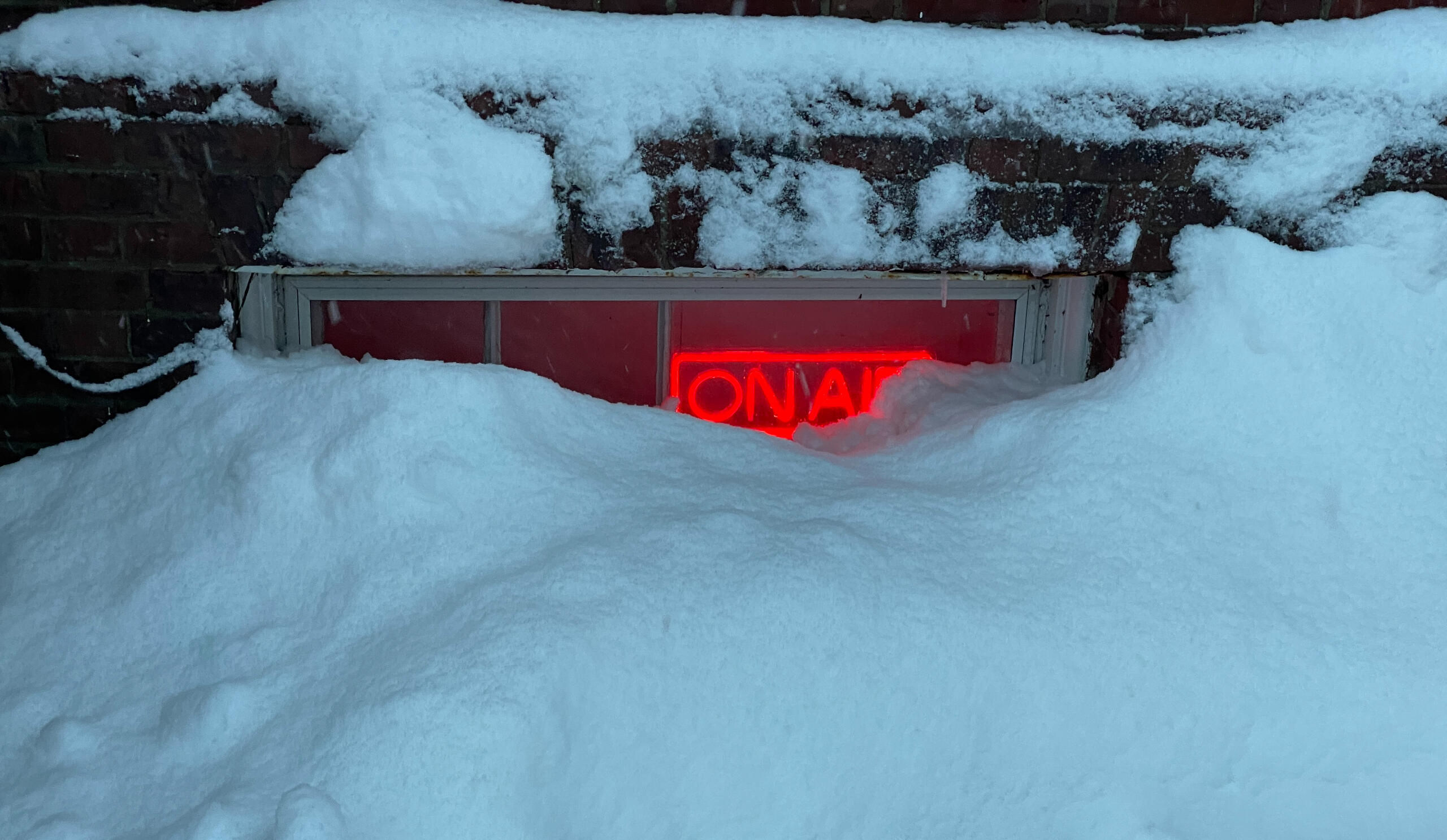 Snow nearly covering the basement window of the record vault, with an on-air sign lit red